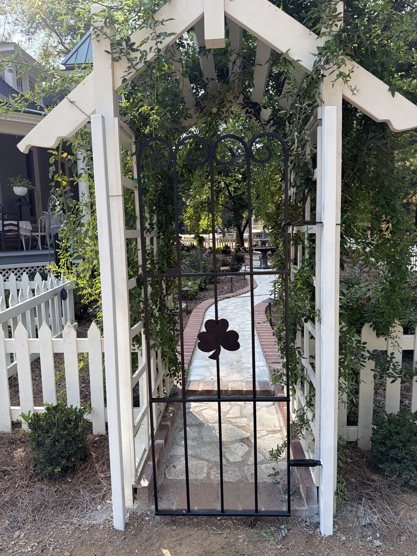 Restored black iron gate with a shamrock and scrollwork beneath a white garden arbor in Franklin, TN